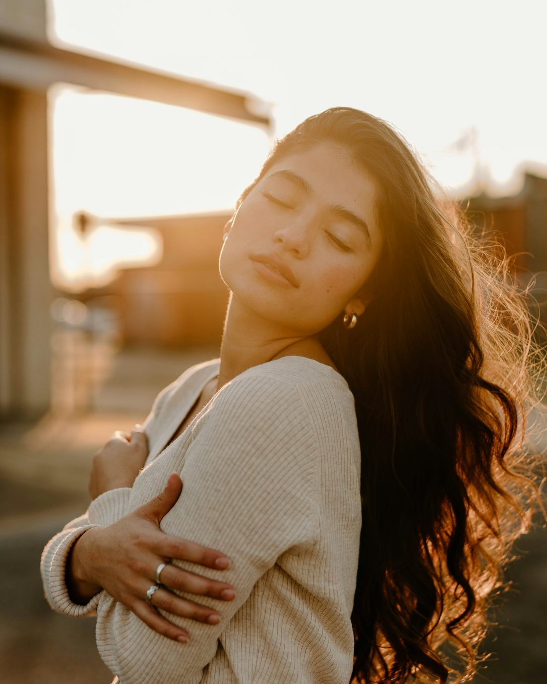 A woman with her eyes closed, holding herself in warm evening light